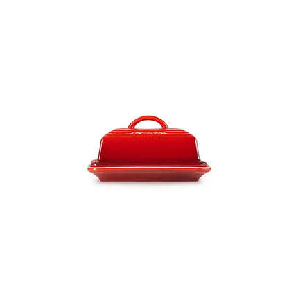 A red ceramic butter dish with a handle on top, sitting on a white background.