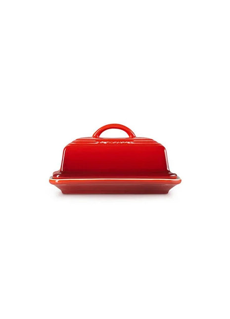 A red ceramic butter dish with a handle on top, sitting on a white background.