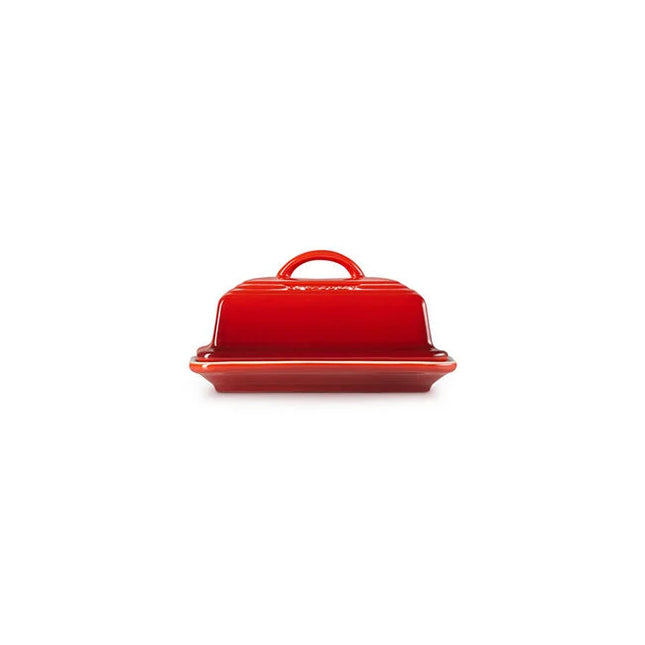 A red ceramic butter dish with a handle on top, sitting on a white background.