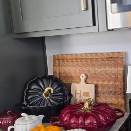 a kitchen counter with various kitchen items, including a wooden cutting board, a white teapot, a black teapot, and a red teapot.