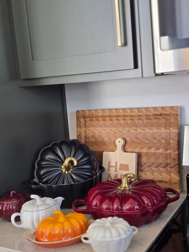 a kitchen counter with various kitchen items, including a wooden cutting board, a white teapot, a black teapot, and a red teapot.