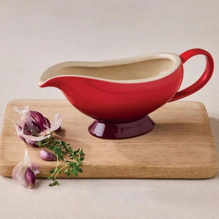 A red crockery bowl with a white interior is placed on a wooden cutting board, accompanied by chopped garlic and herbs.