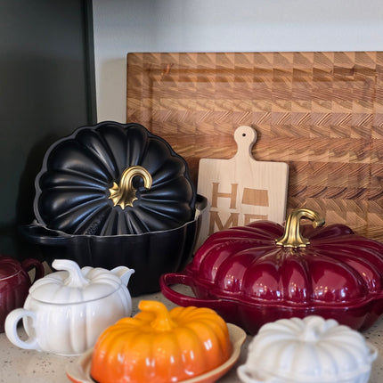 a collection of kitchen utensils and containers, including a wooden cutting board, a black pot lid, a red pot lid, a white teapot, and a wooden tray.