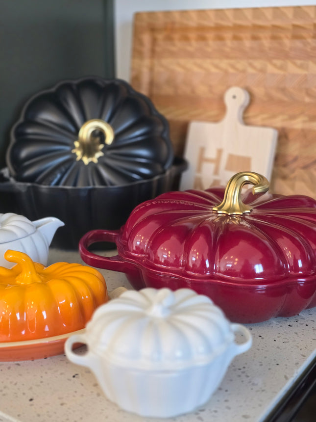a collection of colorful ceramic kitchenware, including a red and gold pot, a black and gold pot, and a white and orange pot, arranged on a kitchen counter.